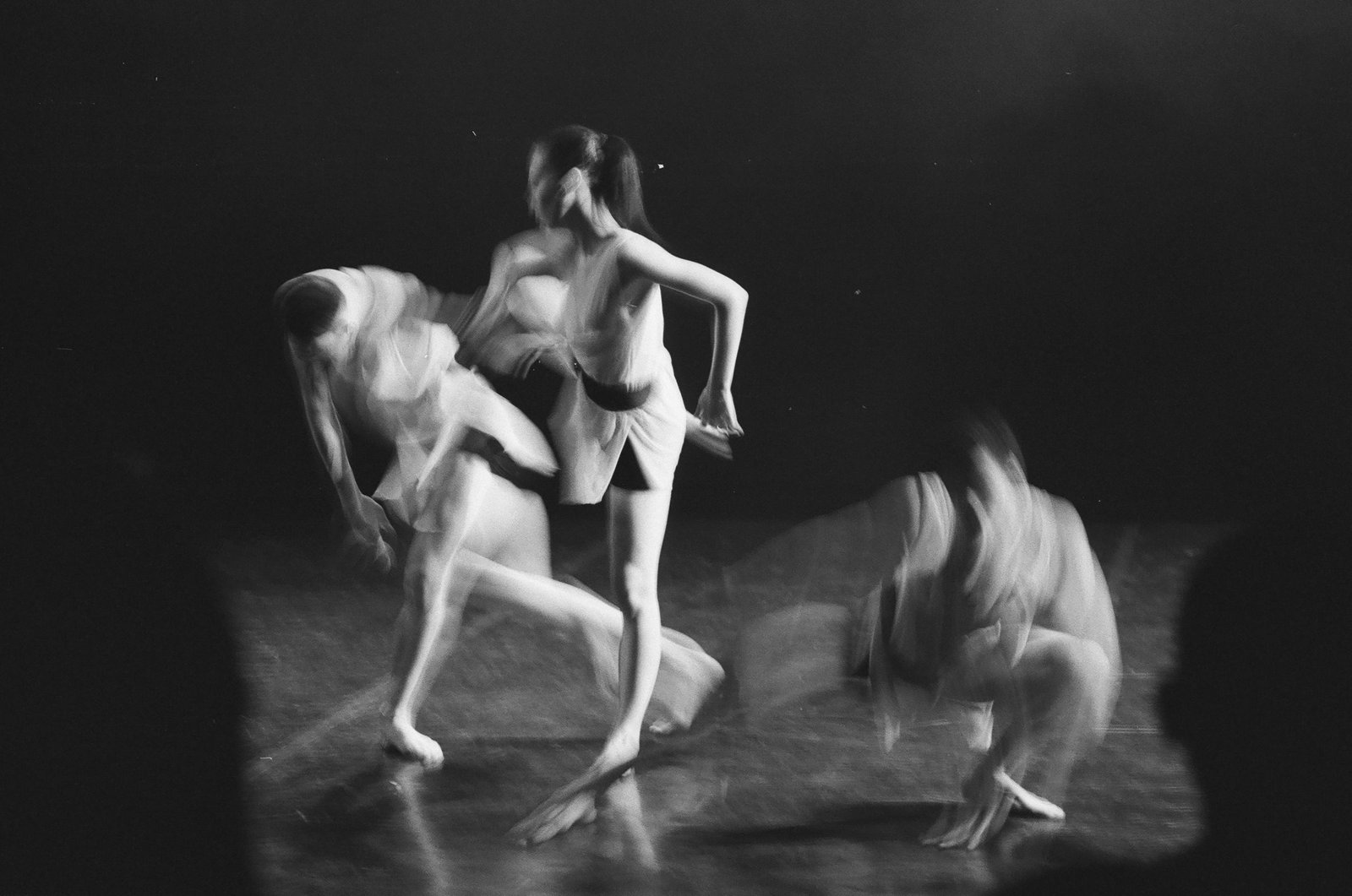 Blurred black and white image of dancers performing energetically on stage.